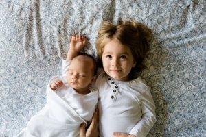 baby laying with older toddler brother on a bed