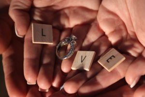 Two hands holding an engagement ring and scrabble letters to spell the word Love.