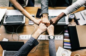 five hands join together to high-five over top of a desk with laptops and other corporate materials