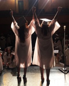 two graduates cheering on stage facing the audience