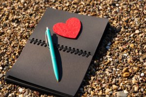 Black paper notebook with red heart and pen.