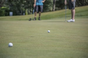 Two men take putts on a golf course green