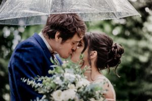 Newly weds share a kiss under an umbrella on a rainy wedding day