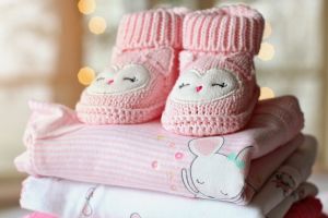 Knitted pink baby booties on top of stack of baby clothes