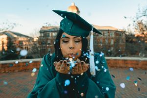 Graduate in cap and gown blowing confetti