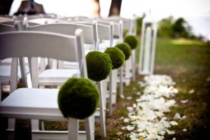 White chairs with green decor line the aisle of an outdoor summer wedding