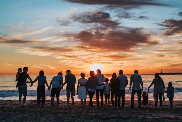 Large family gathered on a beach for a reunion overlooking the water at sunset