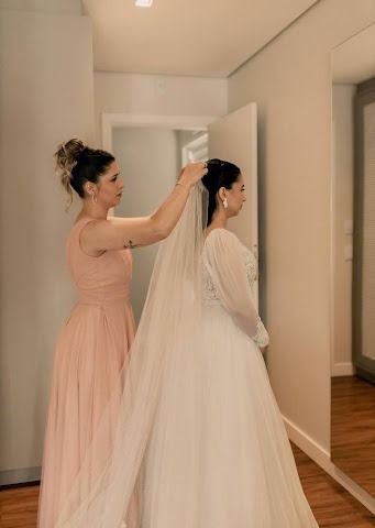Maid of Honor adjusting the bride's veil in a softly lit room before the wedding ceremony.