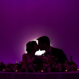 kissing wedding couple seated at the sweetheart table with purple uplighting at a wedding venue in in Lansdale PA 