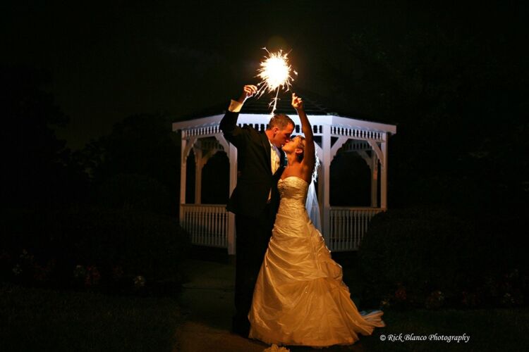 Wedding couple pose with sparklers in front of PineCrest's gazebo at night.