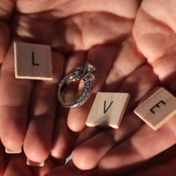 Two hands holding an engagement ring and scrabble letters to spell the word Love.