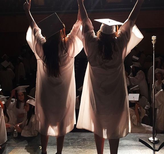 two graduates cheering on stage facing the audience
