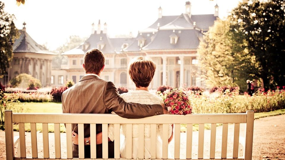 Wedding couple sitting on a bench looking at their reception hall building.