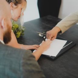 A couple signing a wedding venue contract with a planner, reviewing details and asking important questions before booking their big day.