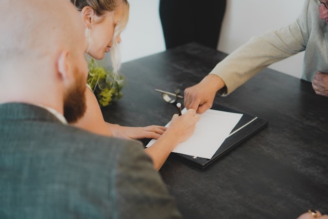 A couple signing a wedding venue contract with a planner, reviewing details and asking important questions before booking their big day.