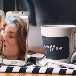two cell phones each with a person in the camera view kissing