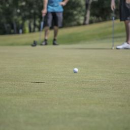 Two men take putts on a golf course green