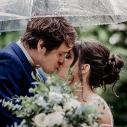 Newly weds share a kiss under an umbrella on a rainy wedding day