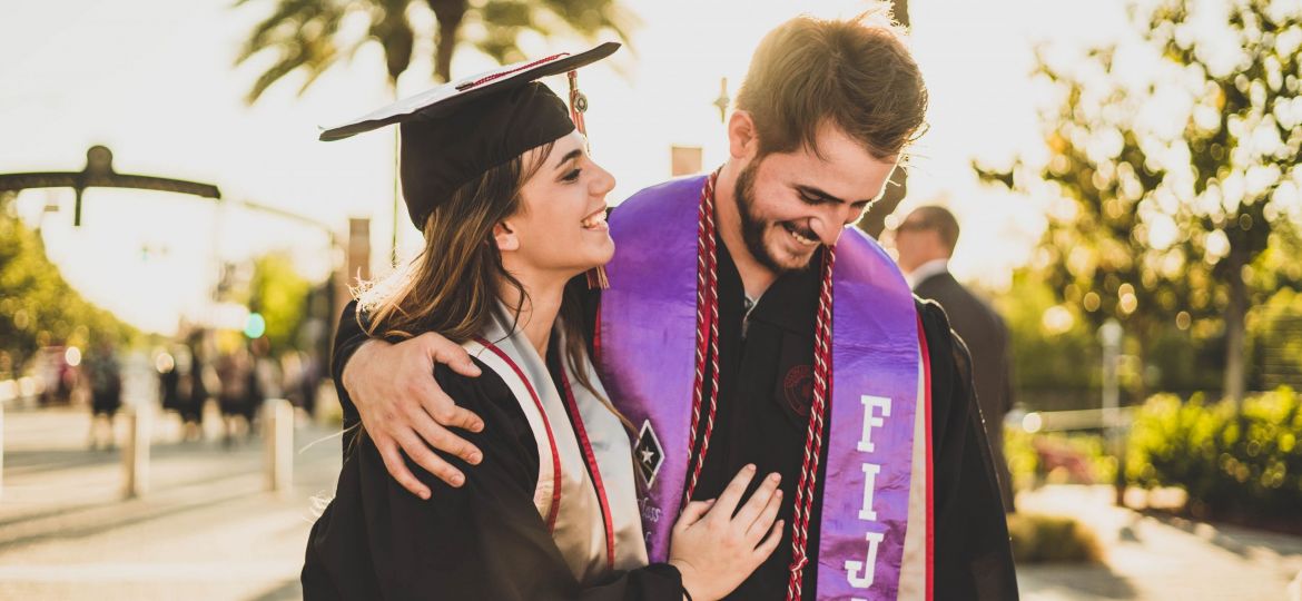 Couple smiling outdoors on a sunny, college graduation day