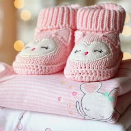 Knitted pink baby booties on top of stack of baby clothes