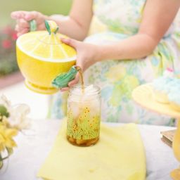Woman in brightly colored dress pours tea out of a yellow teapot