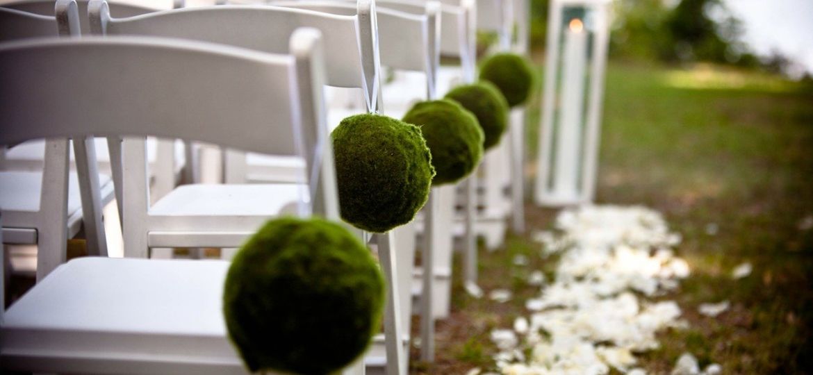 White chairs with green decor line the aisle of an outdoor summer wedding