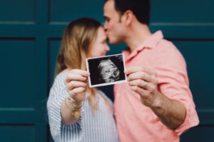 Pregnant couple joyfully holding up a photo of a sonogram