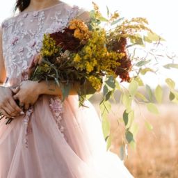 Bride standing in a field holding a fall wedding bouquet