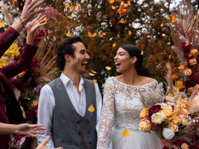 Bride and groom laughing as guests toss fall leaves during an outdoor autumn wedding ceremony, surrounded by vibrant seasonal florals and foliage.