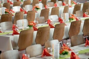 Rows of tables with white cloths and wooden chairs and orange napkins