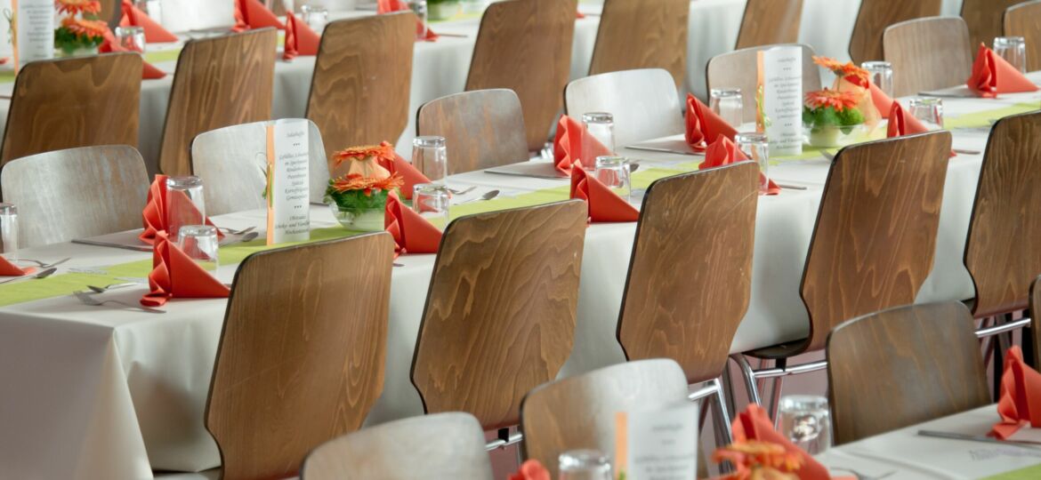 Rows of tables with white cloths and wooden chairs and orange napkins