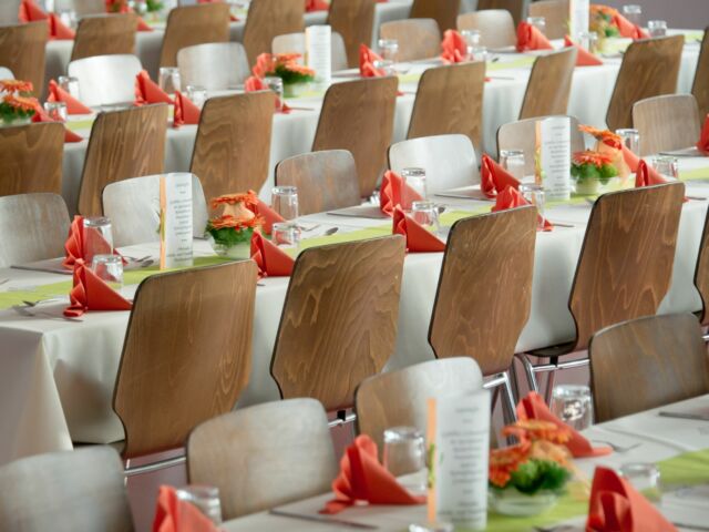Rows of tables with white cloths and wooden chairs and orange napkins