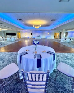 Elegant wedding reception space with blue uplighting, a central dance floor, and round tables set with white linens and navy napkins at PineCrest Country Club, a local wedding venue.