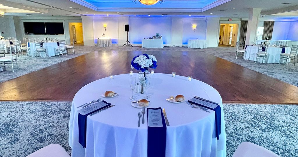 Elegant wedding reception space with blue uplighting, a central dance floor, and round tables set with white linens and navy napkins at PineCrest Country Club, a local wedding venue.