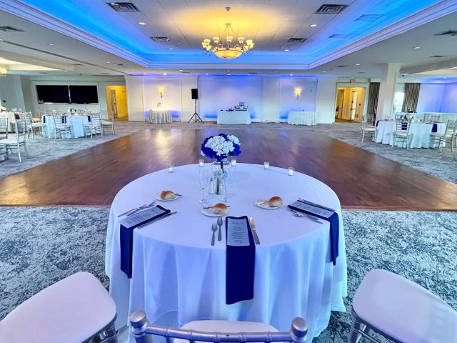 Elegant wedding reception space with blue uplighting, a central dance floor, and round tables set with white linens and navy napkins at PineCrest Country Club, a local wedding venue.