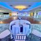 Elegant wedding reception space with blue uplighting, a central dance floor, and round tables set with white linens and navy napkins at PineCrest Country Club, a local wedding venue.
