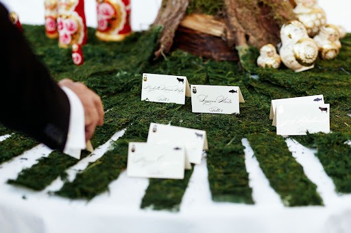 Wedding place cards displayed on a moss-covered table with a guest reaching for their name card, decorated with rustic and woodland-themed elements
