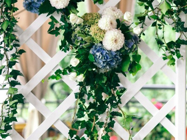 Wedding photo backdrop idea featuring a white lattice panel with cascading greenery and blue and white floral arrangements.